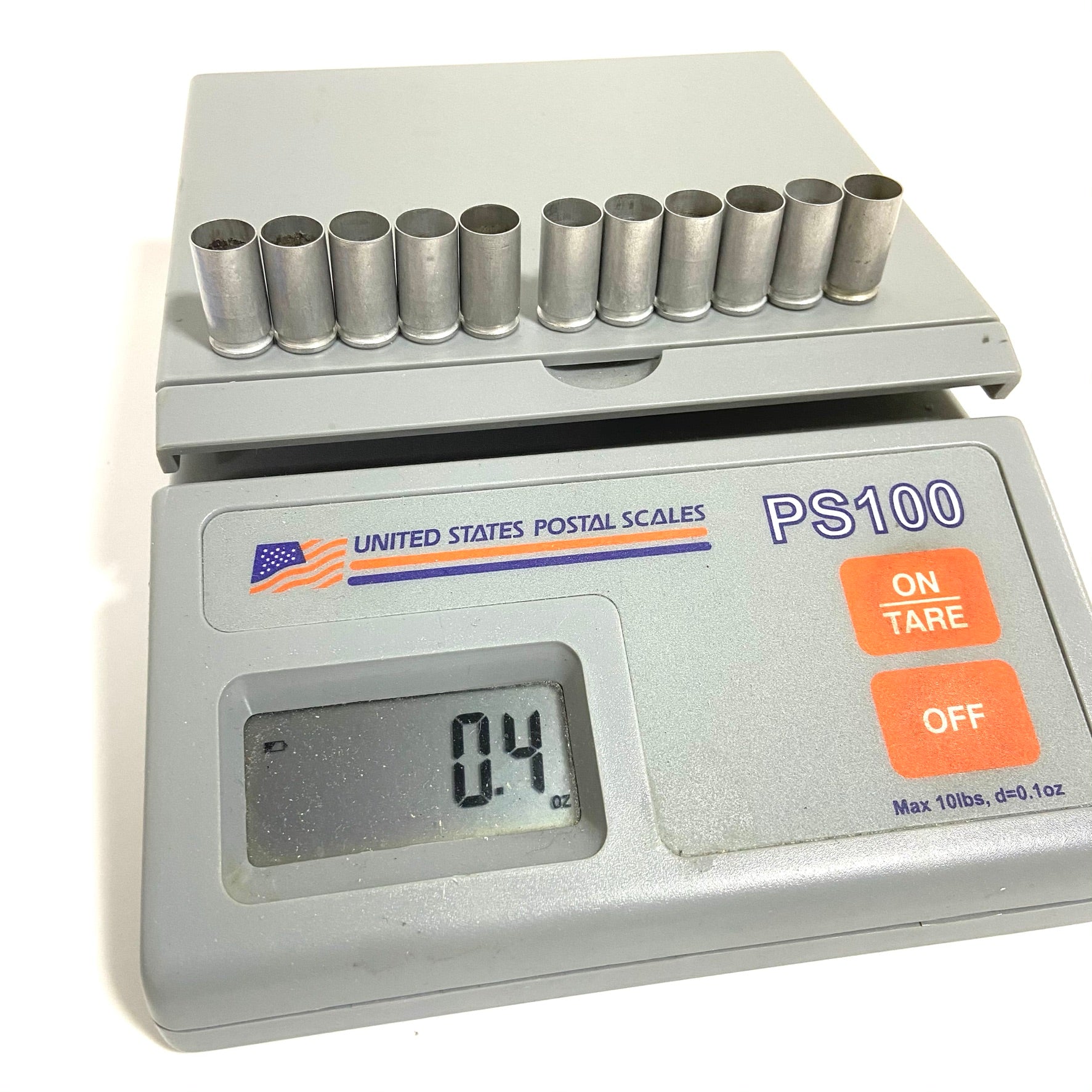 11 silver aluminum 9mm empty shells rest on a digital postal scale displaying 0.4 ounces.