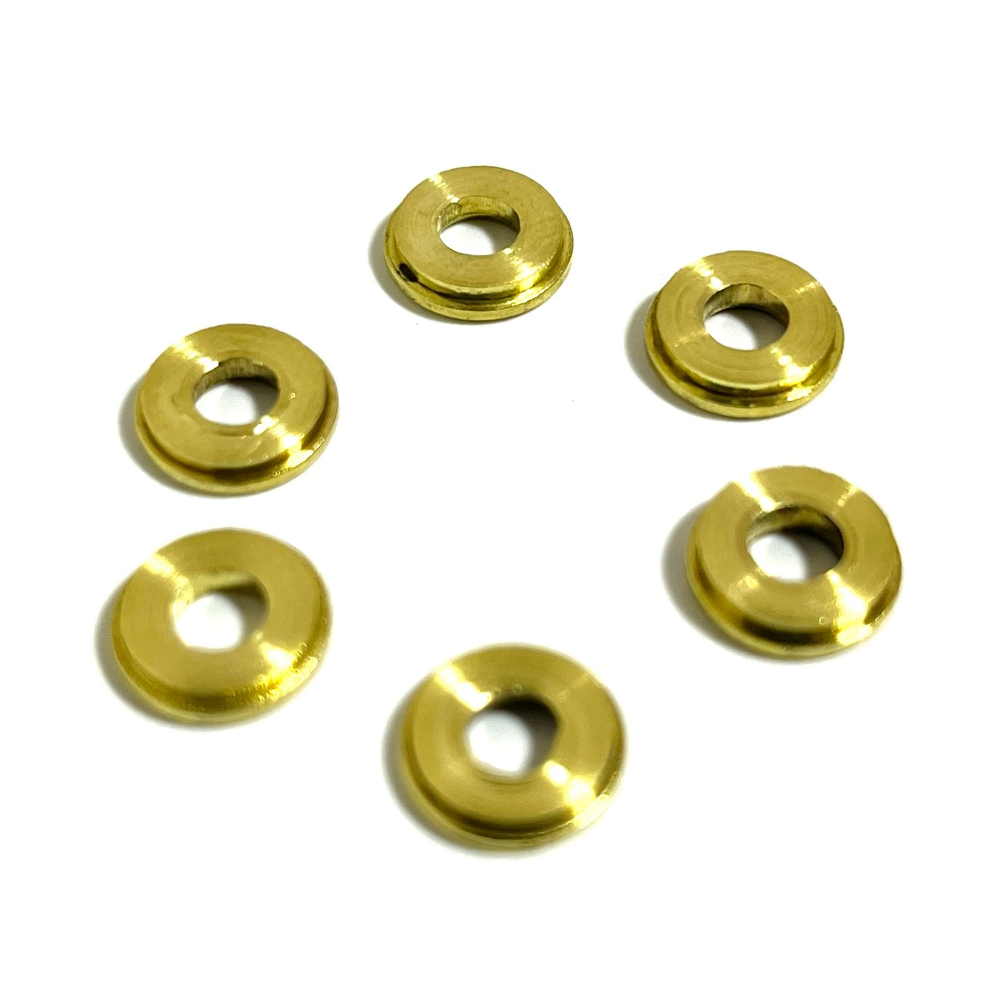 Six used 9mm brass slices with deprimed centers show their smooth back sides, arranged in a loose circle.