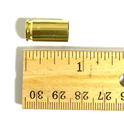 Once-fired brass 9mm cartridge case resting above a centimeter ruler for scale, on a white background.