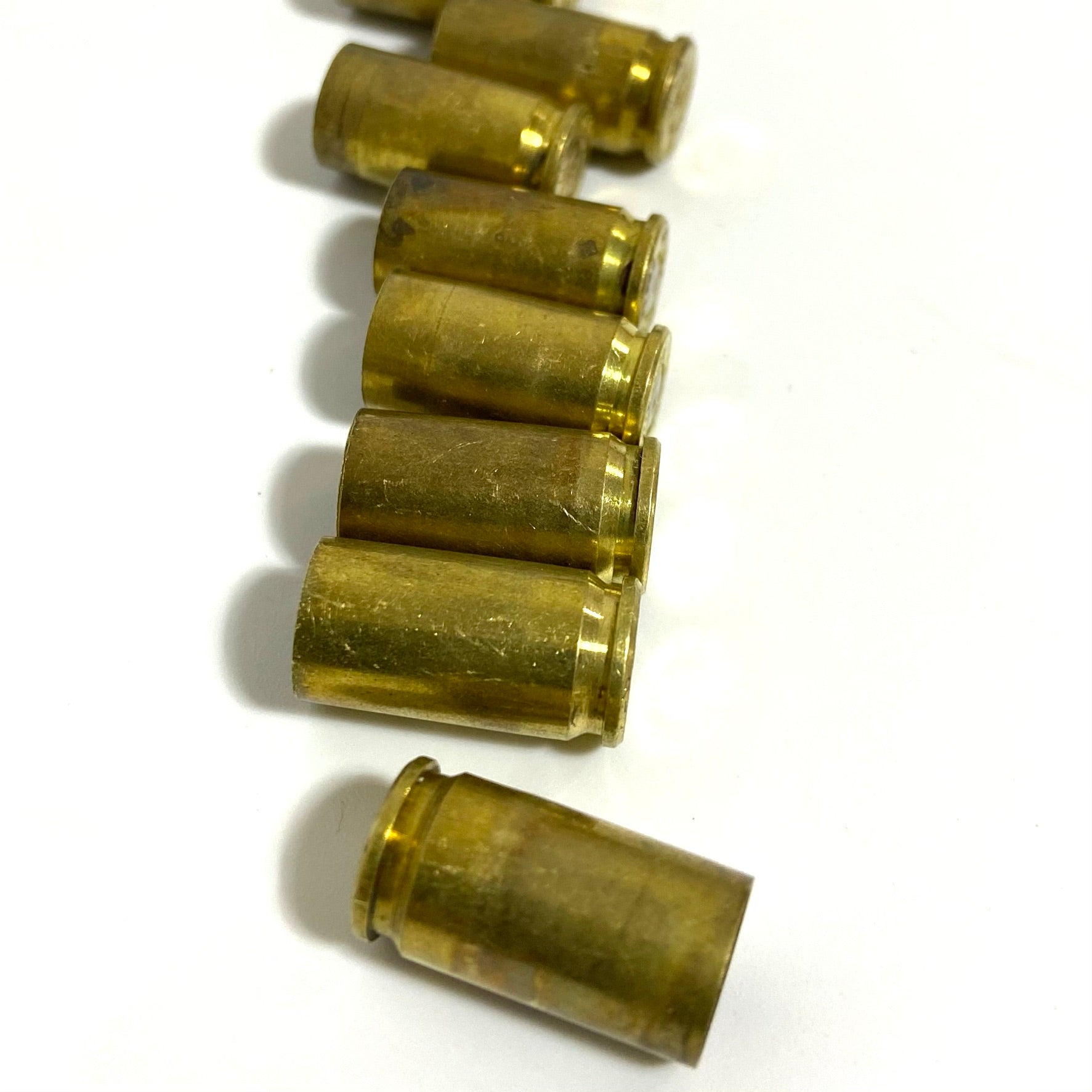 Seven uncleaned 9mm brass shells on a white background with six stacked vertically and one below.