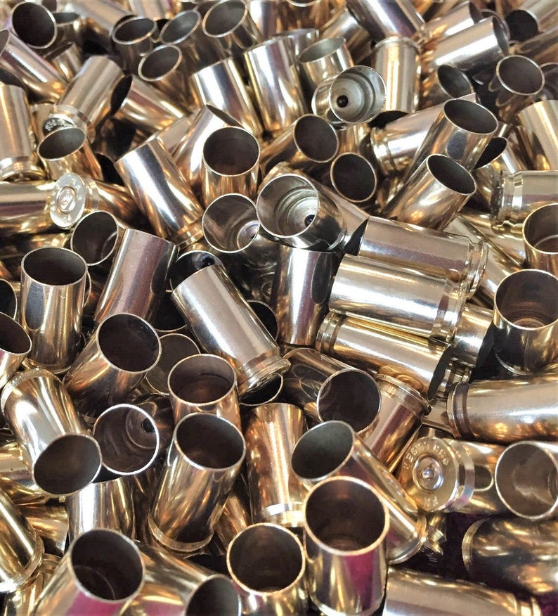 Close-up pile of polished 9mm brass shells showing spent primer dimples and open mouths.

