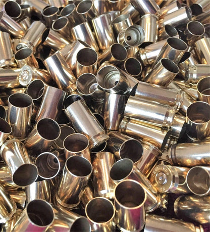 Close-up pile of polished 9mm brass shells showing spent primer dimples and open mouths.
