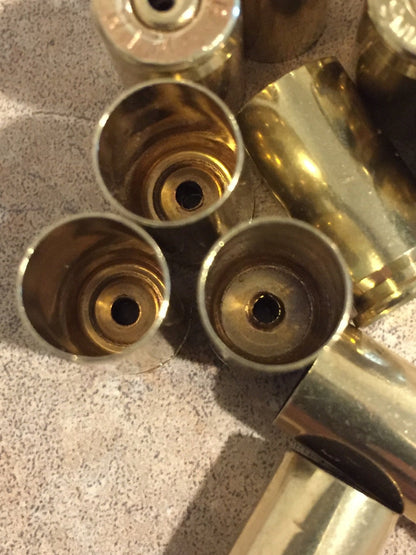 Close-up of three polished brass 9mm casings showing small drilled holes at their bases