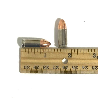 Two inert 9mm cartridges, with one standing upright and one lying horizontally, are displayed on a vintage wooden ruler.