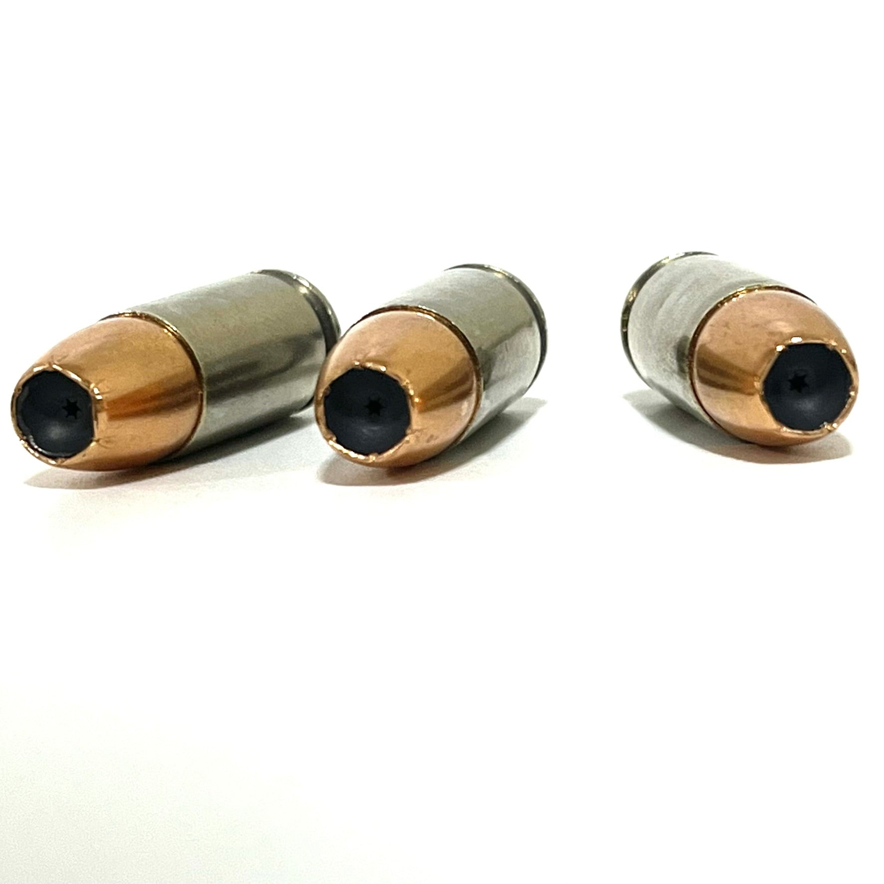 Three inert 9MM Luger nickel dummy rounds lying horizontally on white background, showing JHP copper bullet tips and polished nickel casings. Completely inert, not ammunition.
