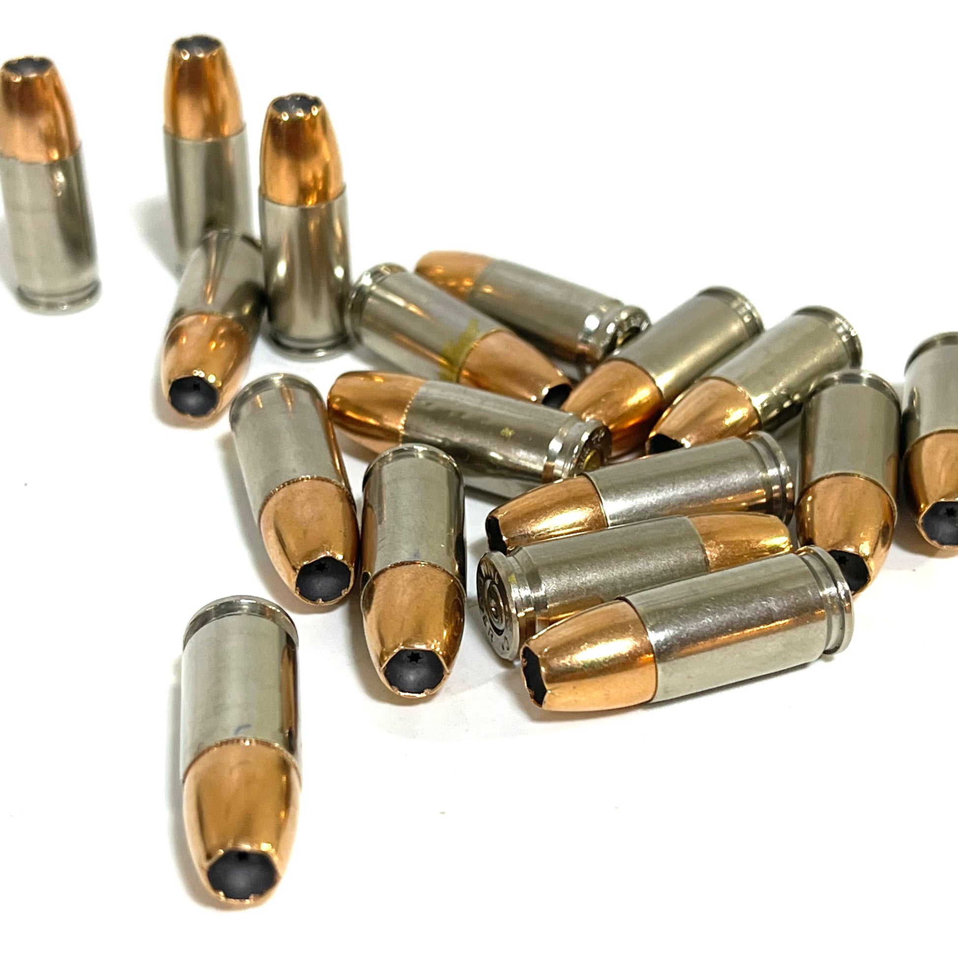 Overhead close-up of multiple inert 9MM Luger nickel dummy rounds showing JHP hollow point cavities, spent primers, and mixed headstamps. Real once-fired brass — not machined replicas.

