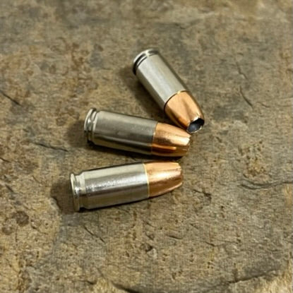 Three inert 9MM Luger nickel-plated dummy rounds with JHP copper bullets arranged on a stone surface. Authentic once-fired casings with natural wear. For cosplay, props, and crafts. 