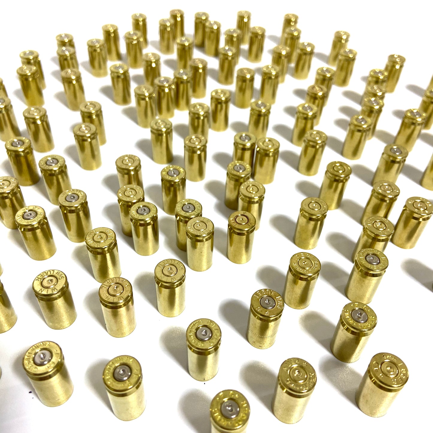 Orderly rows of polished 9mm brass shells standing base up, showing spent primer dimples.
