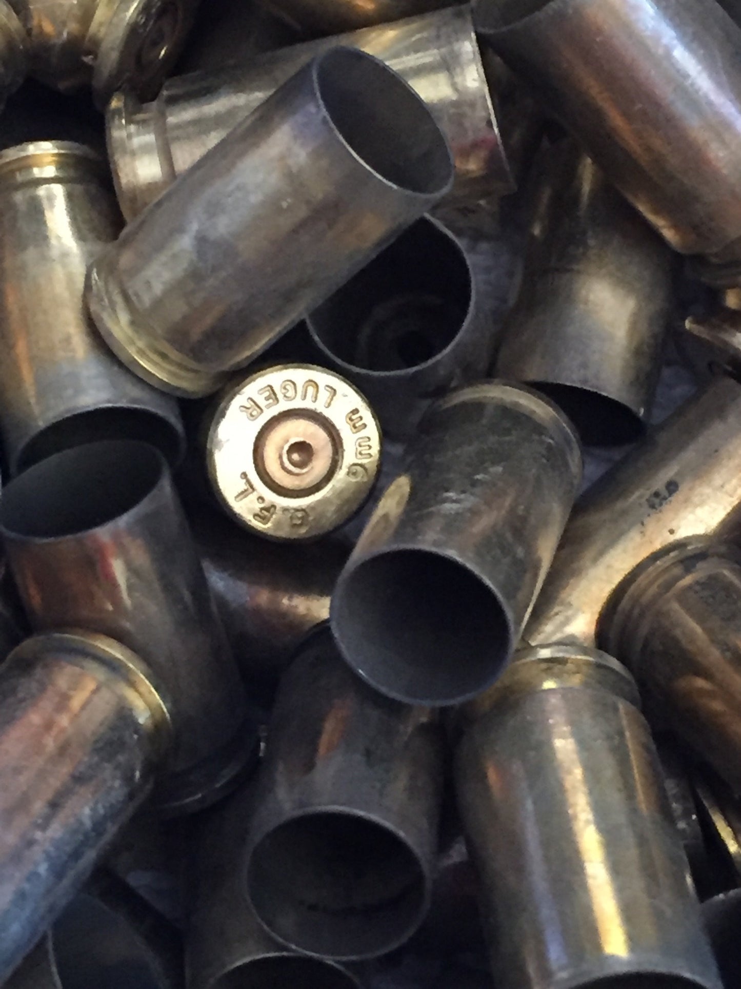 Closeup of a pile of tarnished gold 9mm brass casings, showing a headstamp marked ‘G.F.L. 9mm Luger’
