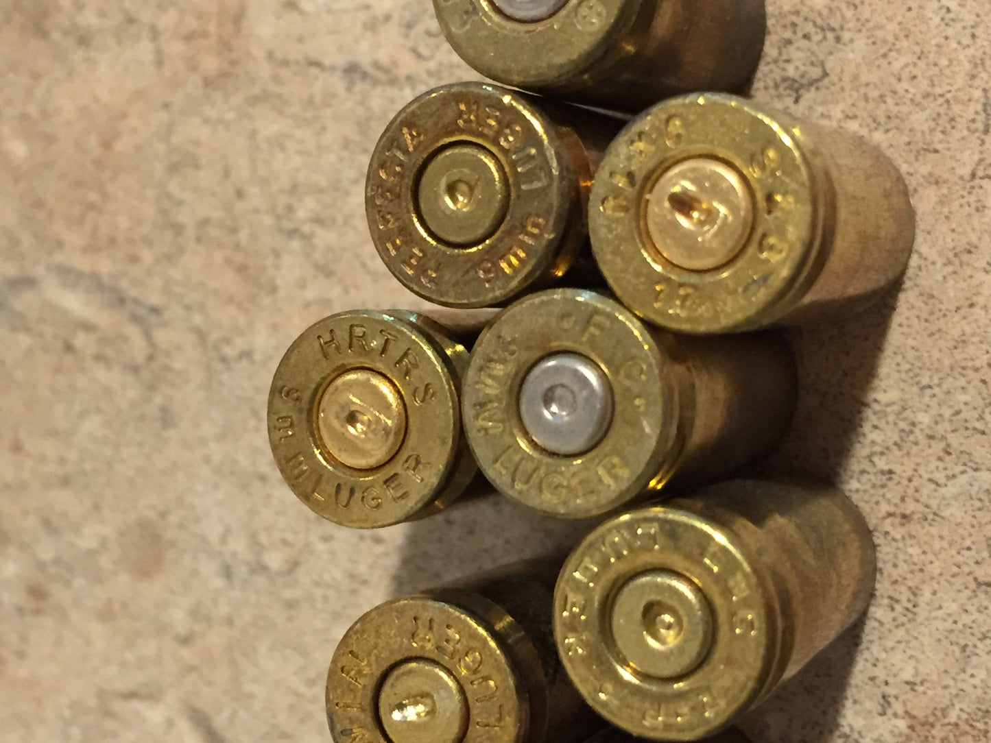 Closeup of gold 9mm brass casing headstamps, showing markings including ‘Federal Luger’, ‘HRTRS Luger’, and ‘Winchester Luger’