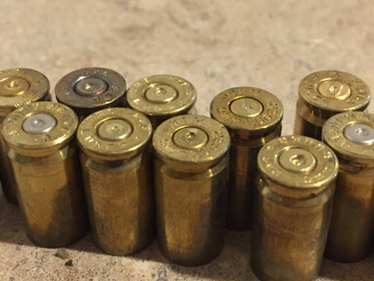 Row of gold 9mm brass casings viewed from above, showing mixed headstamp markings including ‘Luger’ and ‘Federal’