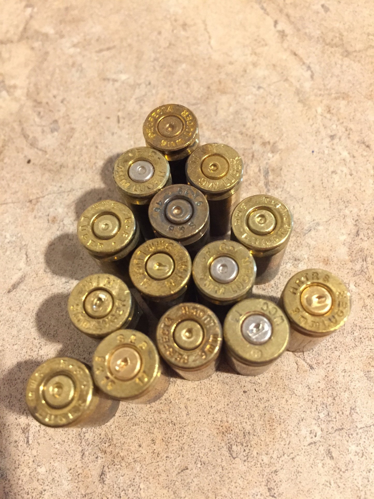 Many gold 9mm brass casings arranged in a triangular pile, viewed from above showing mixed headstamp markings