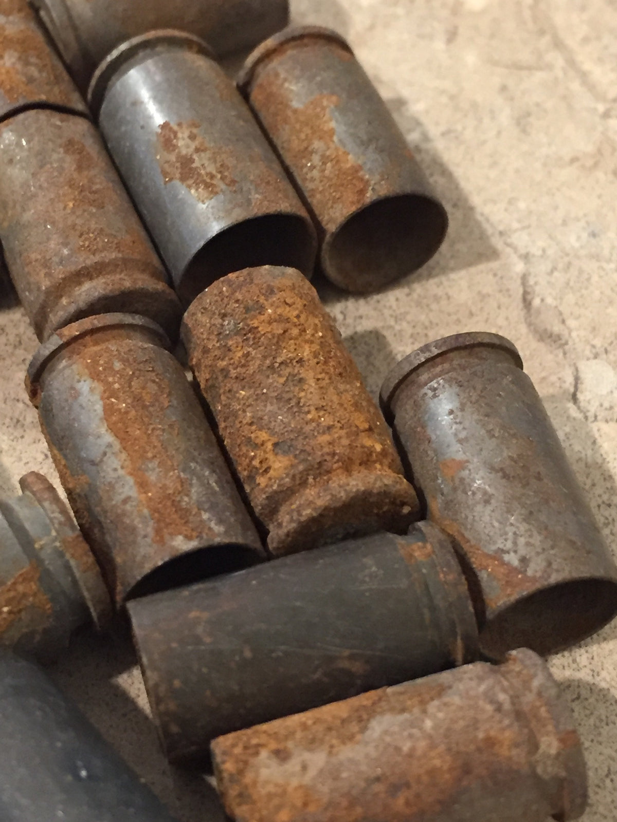 Rusted 9mm casings lying open-end forward in overlapping rows, rust and corrosion covering brass