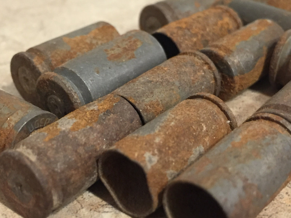 Close-up of rusted 9mm casings with headstamp marking partially visible, heavy corrosion texture