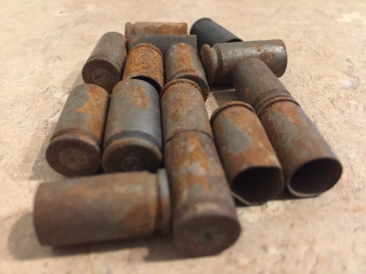 Group of rusted 9mm brass casings on tile, some standing upright showing spent primer pockets