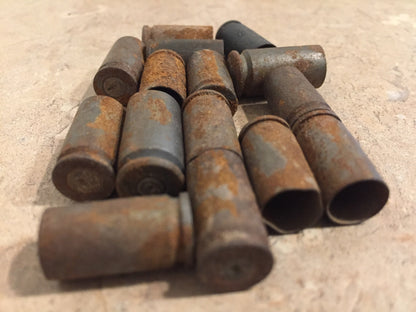 Group of rusted 9mm brass casings on tile, some standing upright showing spent primer pockets