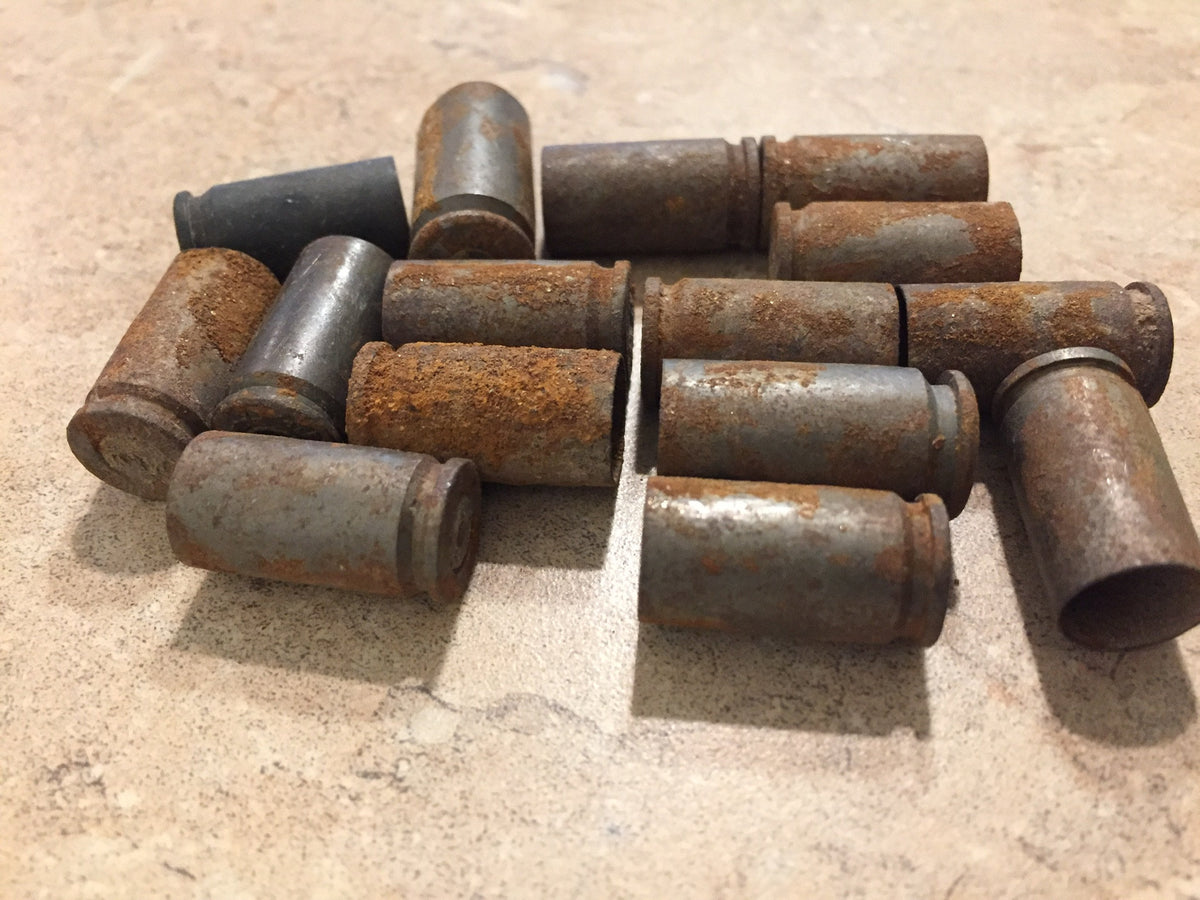 Pile of rusted 9mm shell casings on tile with one dark unrusted casing mixed in