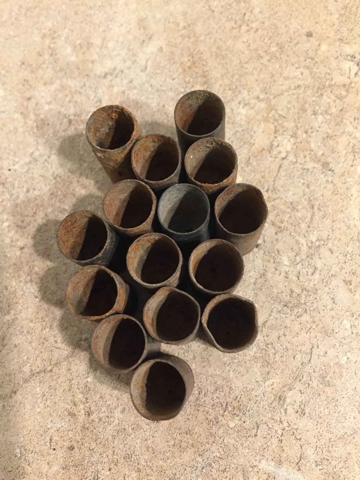 15 rusted 9mm casings standing open-end up viewed from above, dark hollow mouths in cluster on tile