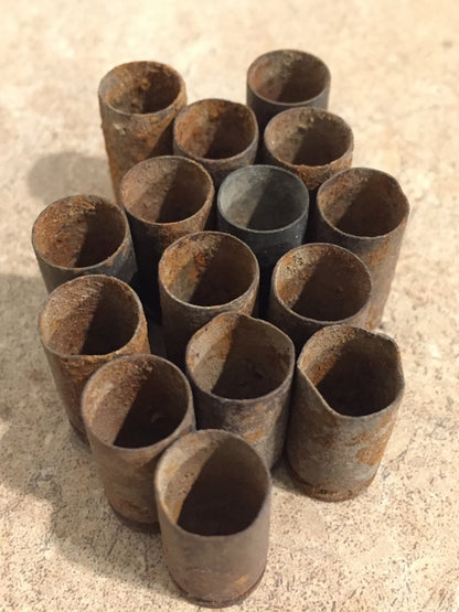 15 rusted 9mm casings standing open-end up in cluster, dark interior mouths visible, heavy rust exterior