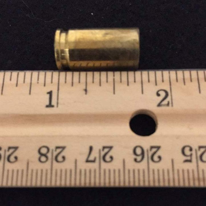 Single spent 9mm brass casing aligned on a wooden ruler showing overall length measurement.