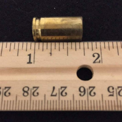 Single spent 9mm brass casing aligned on a wooden ruler showing overall length measurement.
