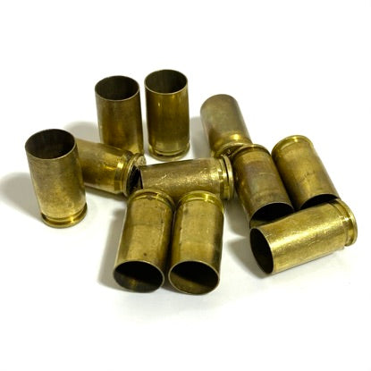 Pile of raw uncleaned 9mm brass shells with mixed tarnish on a white background for bulk crafting.