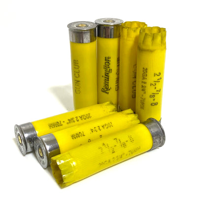 7 yellow Remington Gun Club 20 gauge shotgun shells clustered together on white, four standing upright and three lying at angles, showing silver primer bases and headstamp text