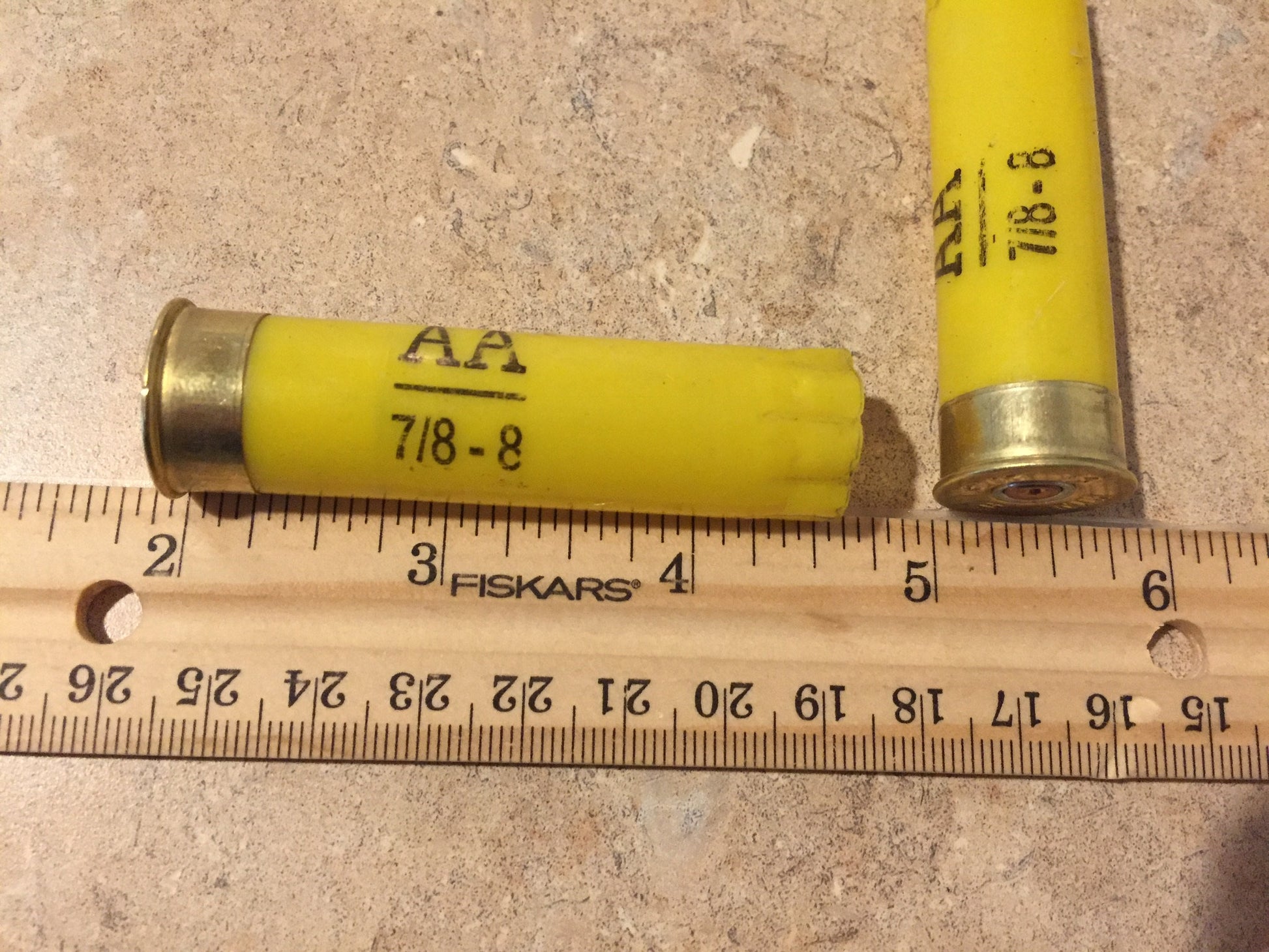 A single empty yellow hull marked 'AA 7/8-8' lies beside a ruler, measuring approximately 2.75 inches.