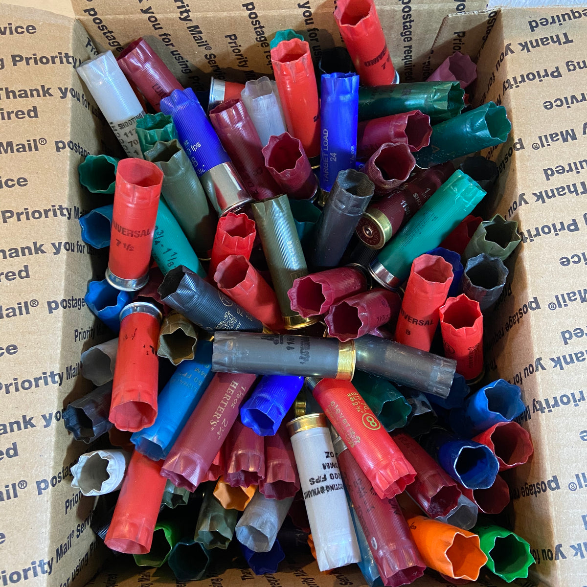 Close-up box of assorted empty shotgun shell hulls showing open crimps and metal bases