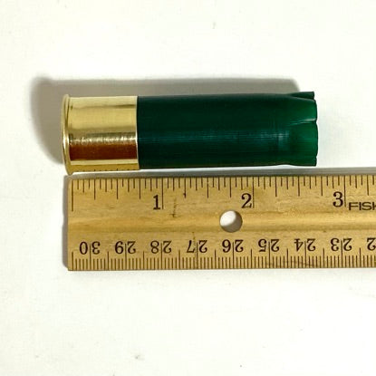 One empty green shotgun shell lying next to a wooden ruler measuring its length.