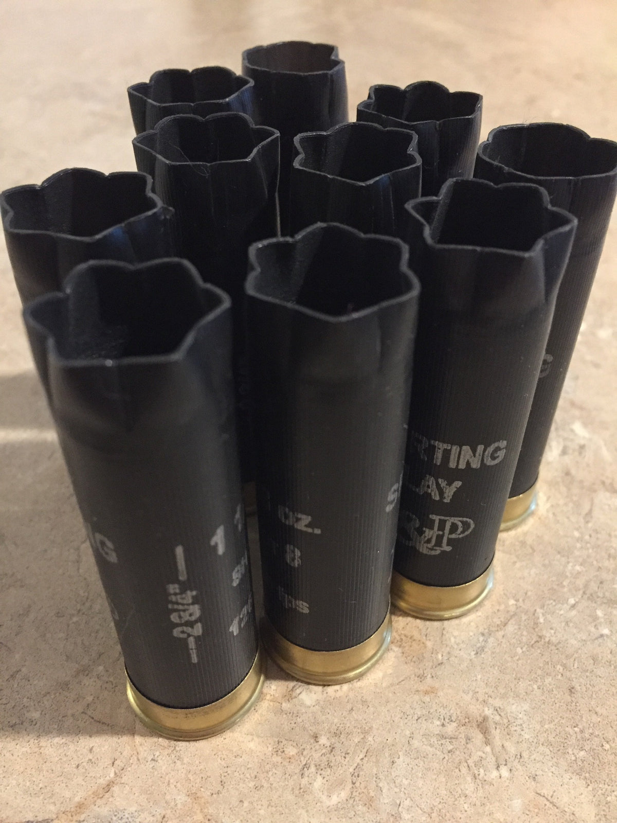 Nine black “B&P Sporting Clay” shotgun shells standing upright with open star-crimped mouths and gold bases