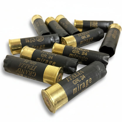 Several black Italia and Mirage shotgun shells scattered and crossed on a wooden surface, showing brass bases.