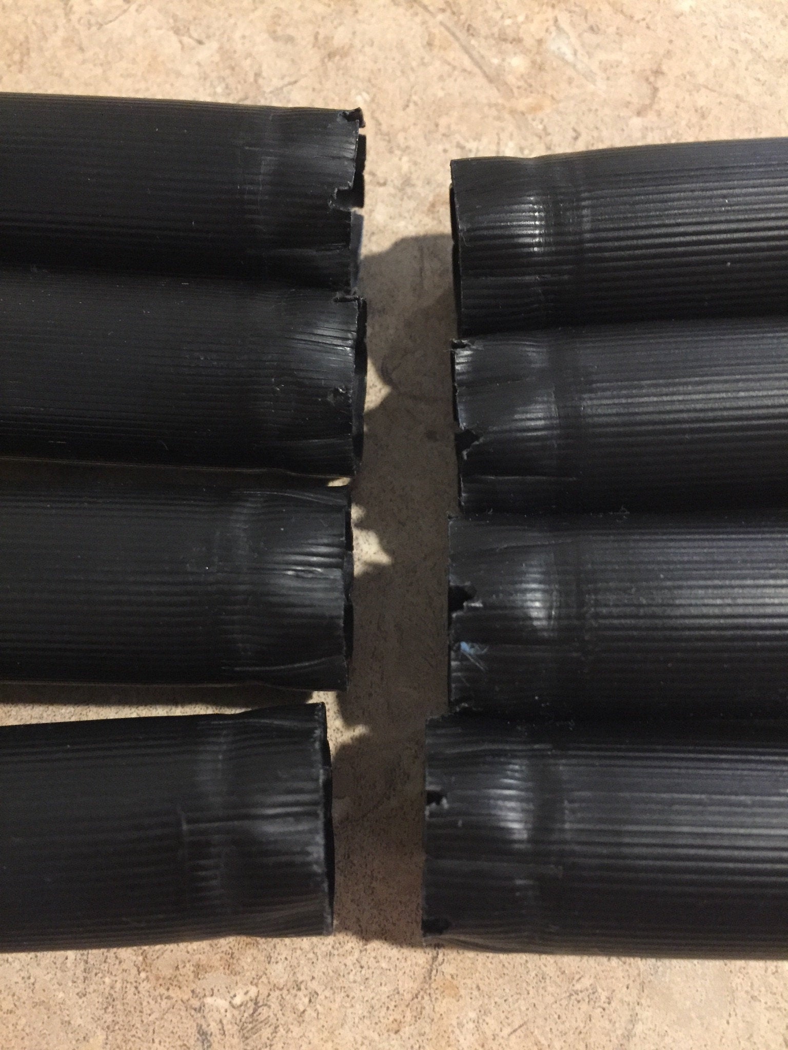 Eight black unmarked cartridges lying on their sides in two rows with closed crimped ends facing forward