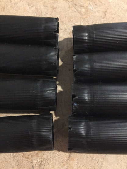 Eight black unmarked cartridges lying on their sides in two rows with closed crimped ends facing forward