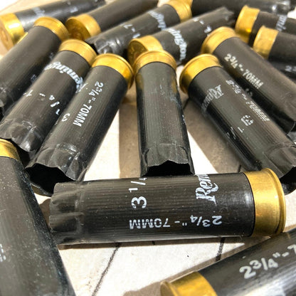 Black 12 gauge empty shotgun shells with gold bases printed 2 3/4 inch 70mm lying on a tile surface