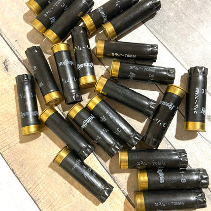 Black 12 gauge empty shotgun shells with gold Remington bases printed 2 3/4 inch 70mm scattered on a wood floor
