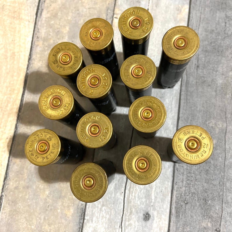 Twelve black 12 gauge empty shotgun shells with gold Remington and Peters headstamps viewed from above on a wood surface
