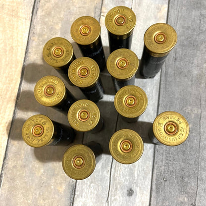 Twelve black 12 gauge empty shotgun shells with gold Remington and Peters headstamps viewed from above on a wood surface
