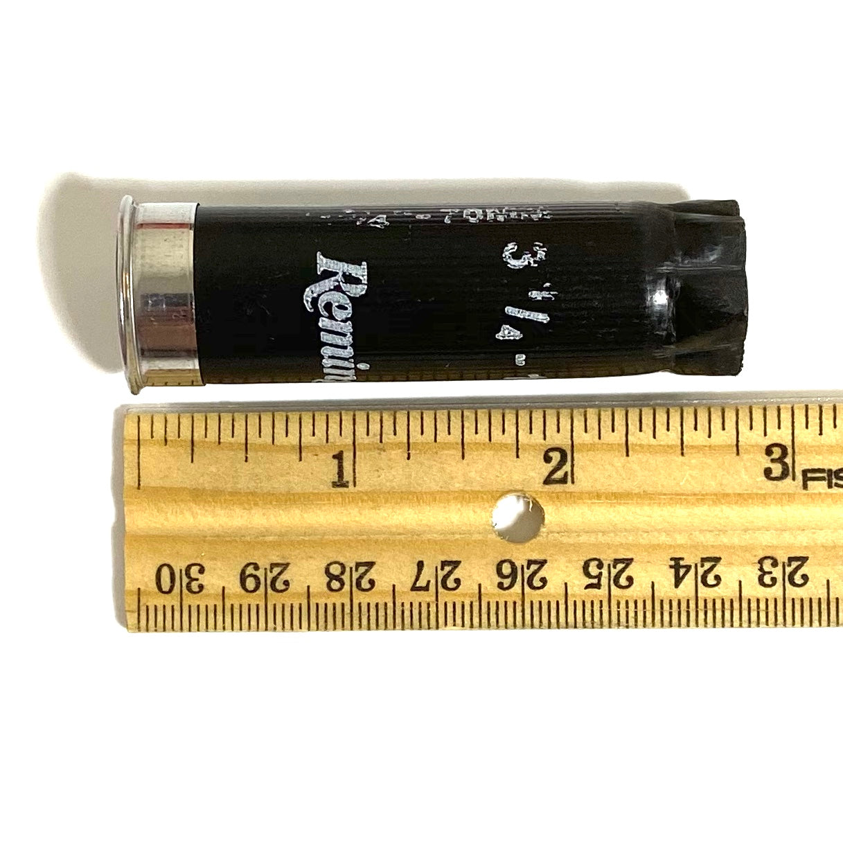 Black Remington 12 gauge shotgun shell lying horizontally next to a wooden ruler measuring approximately 2.75 inches.