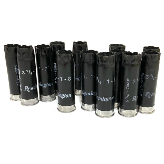 Group of black Remington 12 gauge spent shotgun shells standing upright on a white background.
