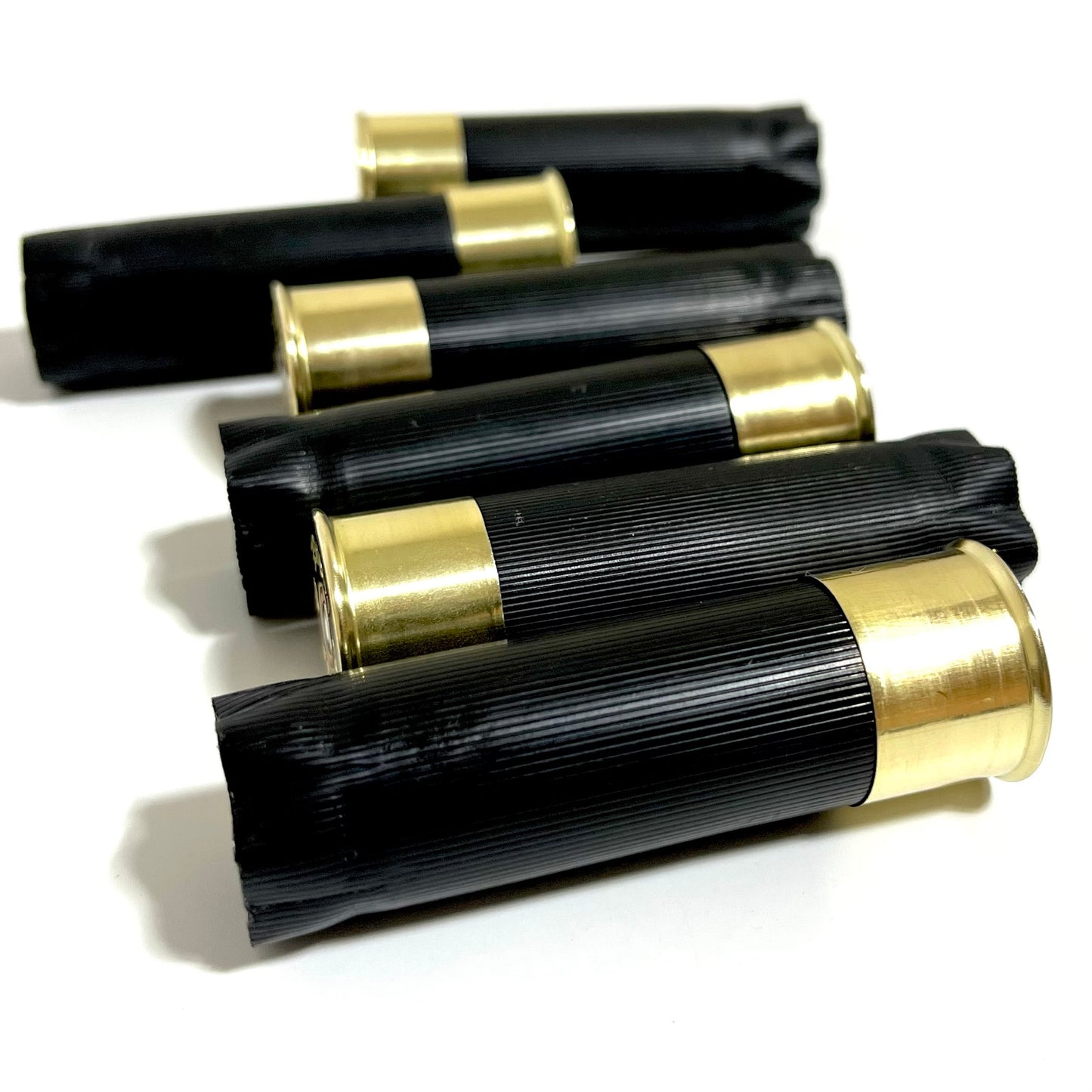 Five black shotgun casings with closed crimped ends and brass bases, fanned in a diagonal row for boutonnieres