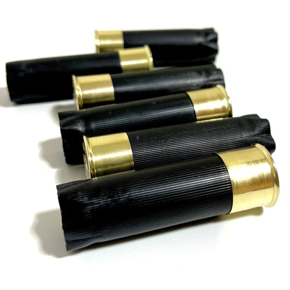 Five black shotgun casings with closed crimped ends and brass bases, fanned in a diagonal row for boutonnieres