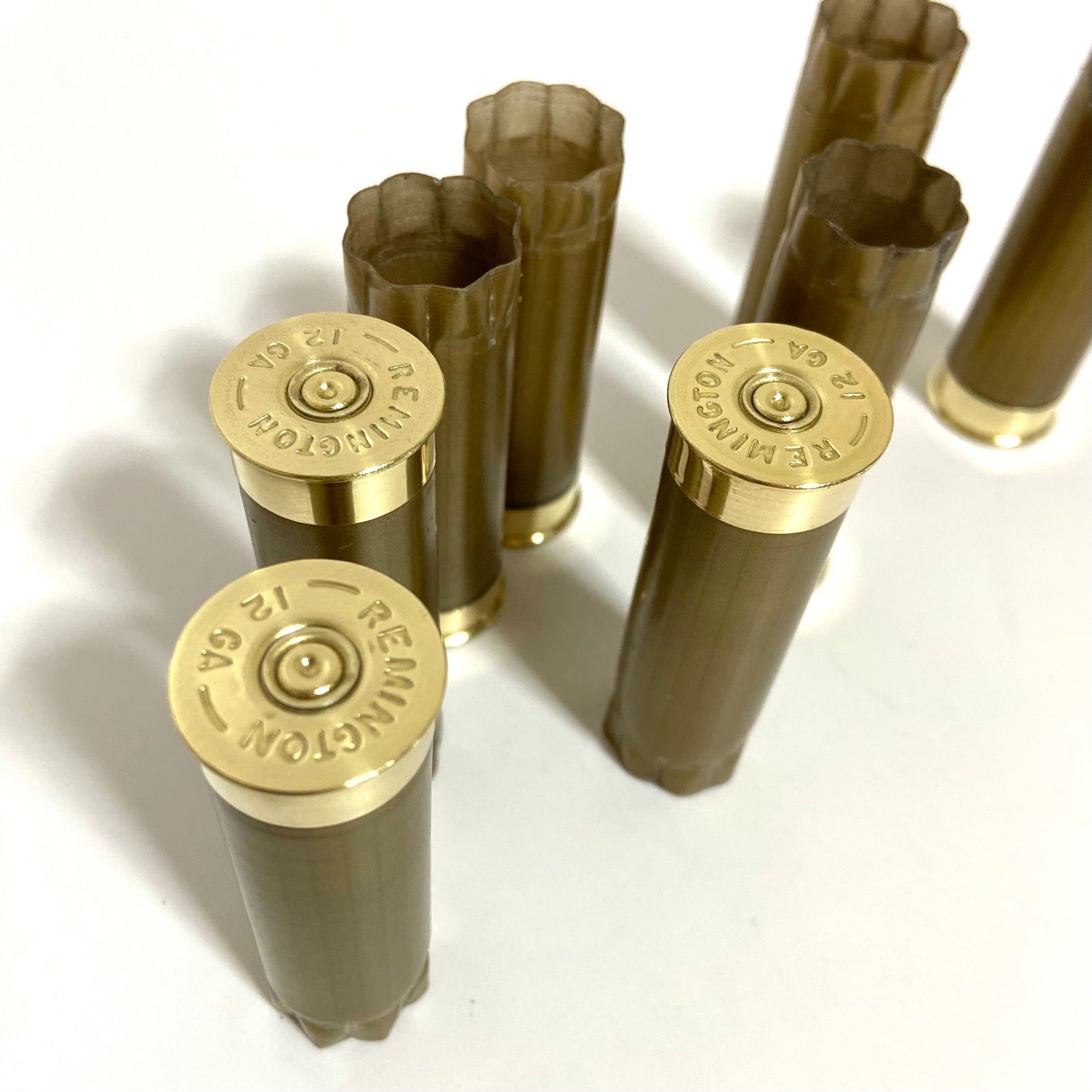 Eight gold blank shotshells standing on a white surface, with three showing readable Remington headstamps.