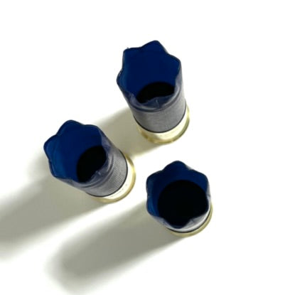 Three blue 12 gauge shotgun hulls standing upright on white, showing open star-crimped top ends and hollow interiors.