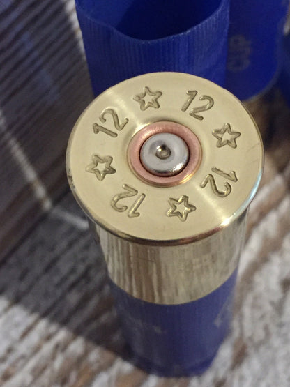 Closeup of a blue shotgun shell base stamped with ‘12’ and star markings around a silver primer