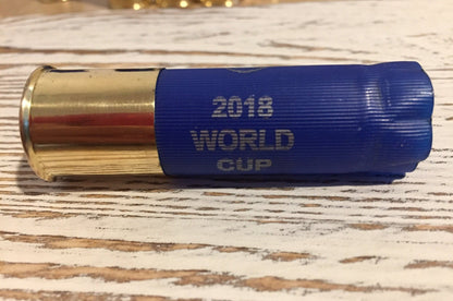 Closeup of a blue ‘2018 World Cup’ shotgun shell with a gold brass base lying on a wood-plank background