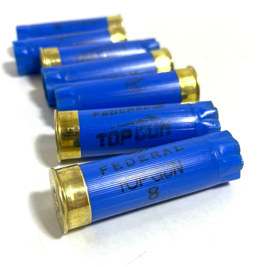 Five blue Federal 12 gauge empty shotgun hulls with gold metal bases arranged side by side white background