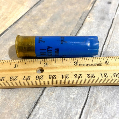 Blue Fiocchi 16 gauge shotgun shell lying next to a wooden ruler showing its length