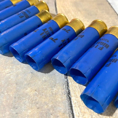 9 blue Fiocchi 16 gauge shotgun shells lying in a row showing open mouths and brass heads on a stone surface