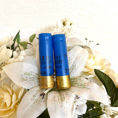 Two blue Fiocchi 16 gauge shotgun shells with brass heads standing among white flowers